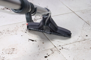 on the white tile floor, a washing vacuum cleaner removes dirty shoe marks after the street, close-up