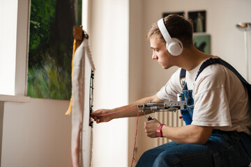 Young white man in headphones working on craft rug with sewing machine