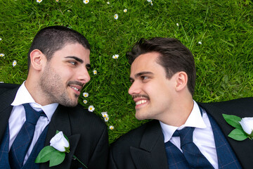 Gay men or husbands lying on grass surrounded by daisy flowers, smiling at each other with room for text