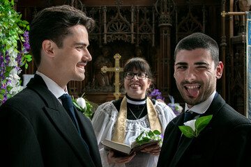 Gay men exchanging wedding rings in front of vicar in church with one groom sticking his tongue out...