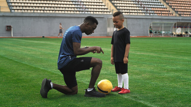 Diverse Trainer And Child Speaking On Football Field