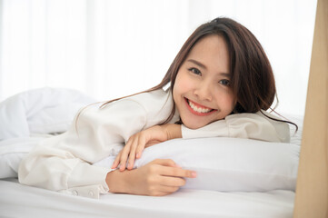 Obraz na płótnie Canvas Young asian woman waking up in the morning on bed. She showing face out the blanket and smile feeling happy