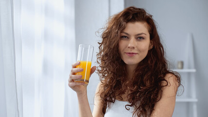 curly young woman holding glass of orange juice at home