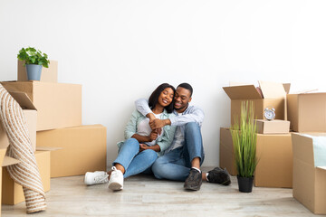 Loving black spouses hugging among moving supplies paper boxes with belongings in empty apartment