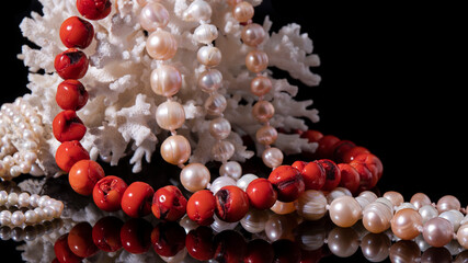 Variety of bright red coral and shiny iridescent pearl necklaces on a black background. Luxurious...