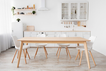 Bright white kitchen with household items. Modern kitchen interior, wooden table and chairs in...