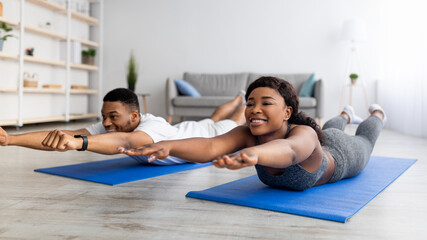 Home trainings during covid lockdown. Strong black couple exercising on sports mats, doing yoga or pilates indoors © Prostock-studio