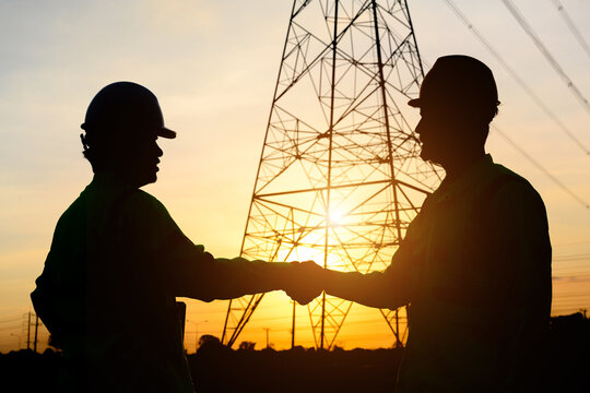 The silhouette of an electrical engineer with a worker Talk to each other and shake hands to agree on the production of electric power. Planned by producing power at the high voltage electrodes.
