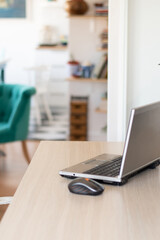 A computer and a mouse stand on a desk in the home office. In the background is the interior of the living room with a blue armchair and a bookshelf