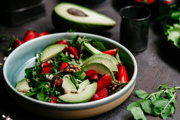 Salad with strawberries, avocado and arugula in a plate on the table. Vegetarian salad