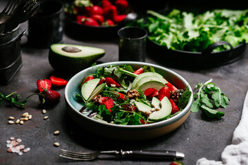 Salad with strawberries, avocado and arugula in a plate on the table. Vegetarian salad
