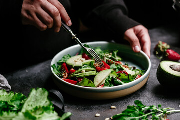 Salad with strawberries, avocado and arugula in a plate on the table. Vegetarian salad