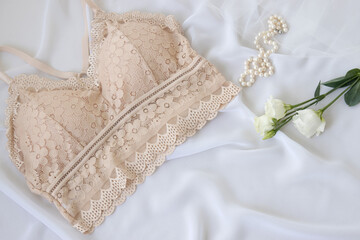 Obraz na płótnie Canvas Woman elegant nude lace bra flowers, jewelry, perfume on a white background. Stylish lingerie flat lay. Underwear fashion concept