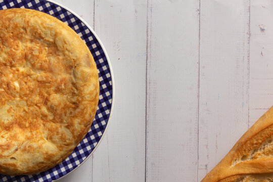 Tortilla de Patatas espa&ntilde;ola. Delicioso plato salado basado en Huevo, Patatas y a veces Cebolla. En fondo de madera blanca, entera y sin cortar. 