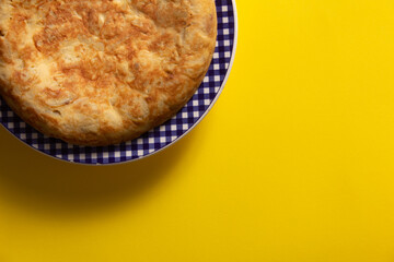 Tortilla de Patatas española. Delicioso plato salado basado en Huevo, Patatas y a veces Cebolla. En fondo amarillo, entera y sin cortar. 