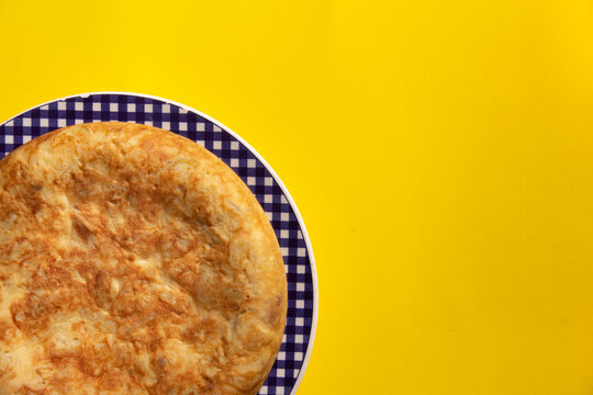 Tortilla de Patatas espa&ntilde;ola. Delicioso plato salado basado en Huevo, Patatas y a veces Cebolla. En fondo amarillo, entera y sin cortar. 