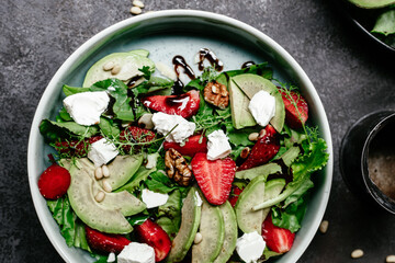 Salad with strawberries, feta, avocado and arugula in a plate on the table. Vegetarian salad