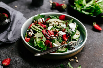Salad with strawberries, feta, avocado and arugula in a plate on the table. Vegetarian salad