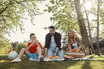 Happy young mother and father with little boy smiling while having picnic outdoors