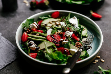 Salad with strawberries, feta, avocado and arugula in a plate on the table. Vegetarian salad