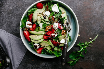 Salad with strawberries, feta, avocado and arugula in a plate on the table. Vegetarian salad