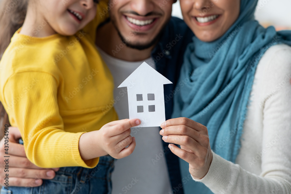 Poster new home. happy muslim family holding cutout paper house figure in hands