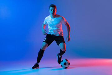 Young Caucasian man, male soccer football player training isolated on gradient blue pink background in neon light