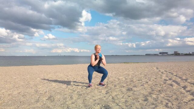 Young caucasian woman doing gym exercises and training on the beach in Amager, Copenhagen, Denmark. The girl is training with a kettle ball. It is a sunny spring evening. Slow motion 4K