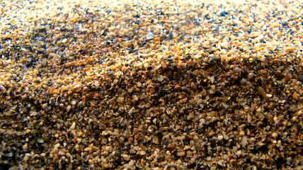 Course sand and small pebbles on a sunny beach, close up