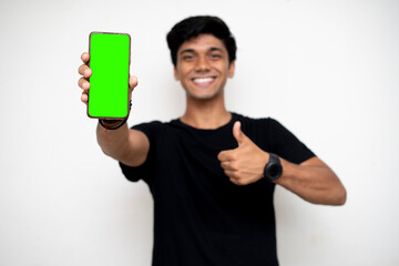 Young indian boy holding a mobile phone and point towards it's screen. Mobile phone with a green screen for mockup.