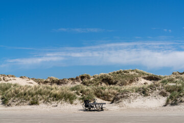 two bicycles parked in front of a large sand dune covered in grasses and reeds under a blue sky