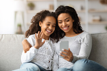Cheerful black mother and daughter having video call via smartphone