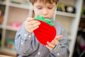 Child plays with strawberry shape sensory fidget toy Pop it. Instrument for fine motoric skils,...