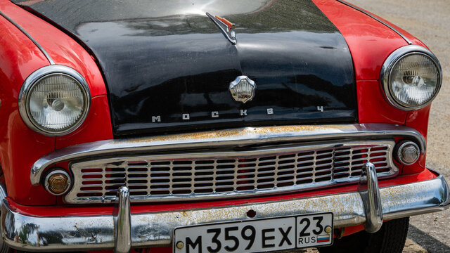 Front part of red retro car Moskvich 407 in Arkhipo-Osipovka. On black hood there is inscription "Moskvich" and logo. Radiator grill is chrome-plated. Krasnodar Territory, Russia - May 16, 2021