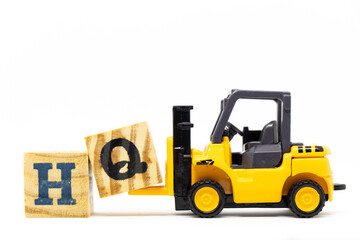 Toy forklift hold letter block q to complete word HQ (Abbreviation of headquarters) on wood background