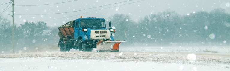 Snow blower car clears the road in the field during a winter blizzard. Lorry closeup. Soft focus