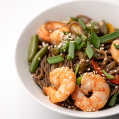 Brown Spaghetti with king shrimp or prawn, vegetables and sesame seeds. Wok Spicy oriental dish, Pan-Asian cuisine. Part of food plate on white background. Soft focus. Close up shot.