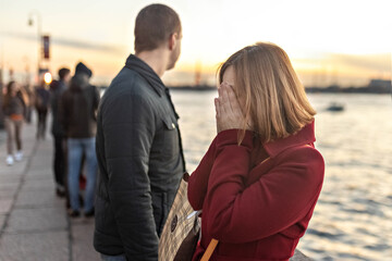 Young couple man and woman in a quarrel, on the embankment of the river in the city at sunset. The girl covered her face with her hands, crying. Emotions