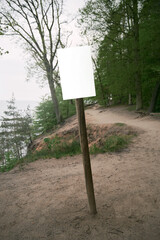 Empty information board on a wooden pole on the forest. Mock up attention sign in national park. Forest warning board.