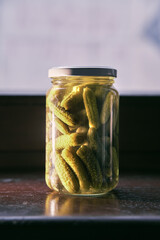 Little jar full of small cornichons. Glass jar with marinated cucumbers