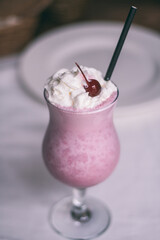 Partially blurred glass with berry milkshake with straw, whipped cream and cocktail cherry. Vertical