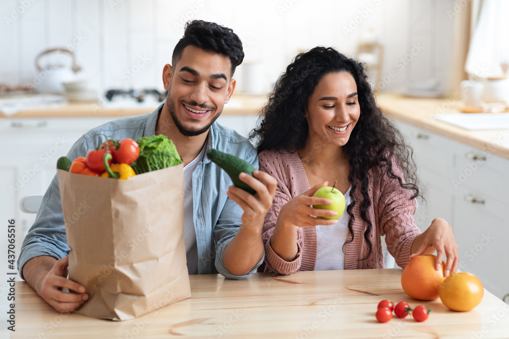 Wall mural Healthy Nutrition. Happy Arab Spouses Unpacking Paper Bags After Grocery Shopping