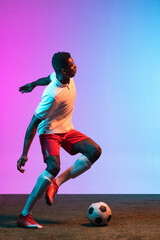 Portrait of African professional football player training isolated on gradient blue pink background in neon light.