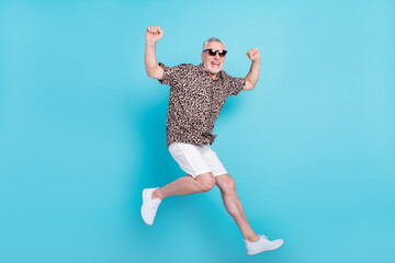 Full body photo of cheerful happy old man wear sunglass jump up air isolated on blue color...