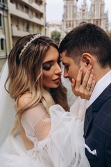 Romantic walk of the bride and groom through the city streets. Newlyweds on the background of the cathedral. Summer day.