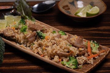 Pork fried rice with broccoli and carrots on wooden background.