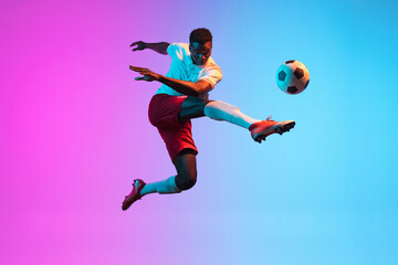 Obraz na płótnie Canvas One African man, professional soccer football player training isolated on gradient blue pink background in neon light.