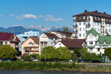 Residential buildings in federal territory of Sirius against backdrop of snow-capped peaks. Caucasus mountains. Imeretinskaya lowland. In foreground is Mzymta.Adler. Sochi, Russia - May 18, 2021