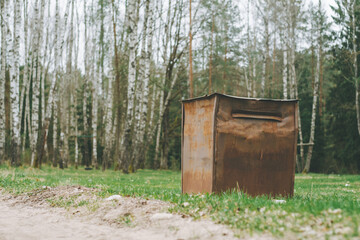 Fototapeta premium Garbage container in countryside, in birch grove. Brown rusty trash can on the grass in forest