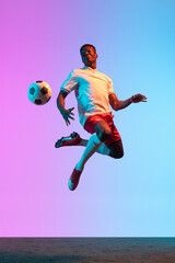 Portrait of African professional football player standing isolated on gradient blue pink background in neon light. Back view © master1305